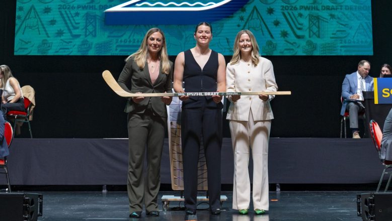 From left to right: Hefford, Dwyer, and Marmer all smile at the camera as they hold a wooden stick in front of a big screen with the Fleet logo on it.