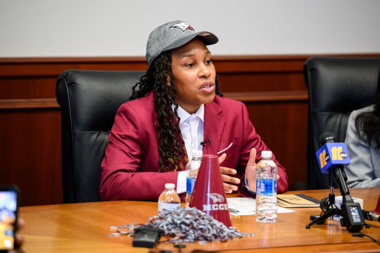Olivia Gaines is wearing a maroon blazer with a gray hat and answering questions.