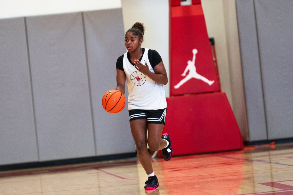 A player in a white and black Houston practice uniform dribbles a basketball on a court. 
