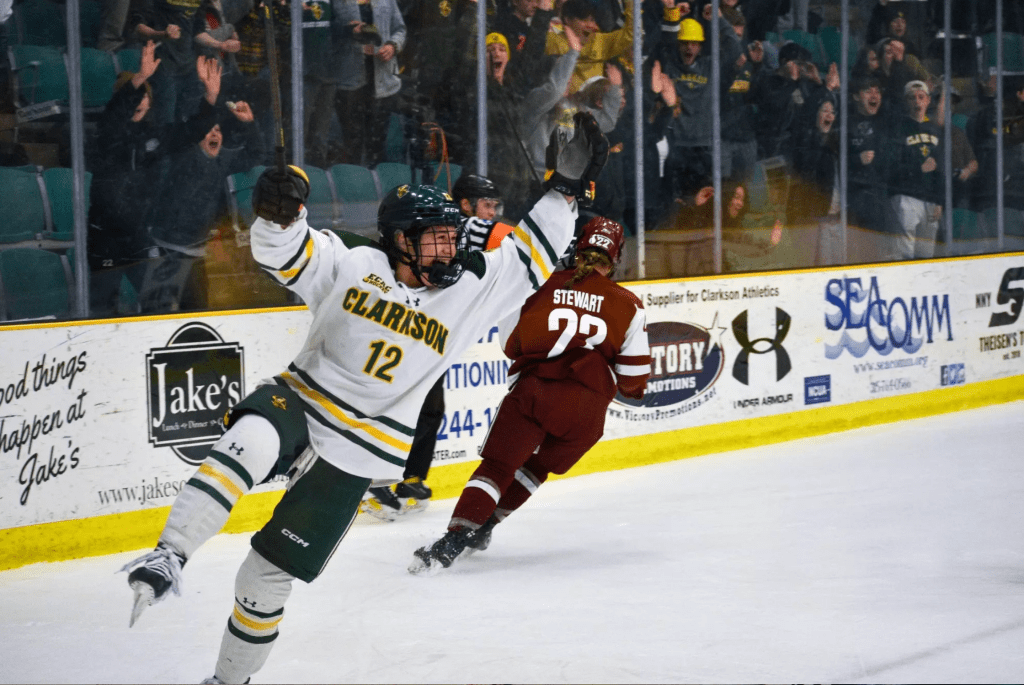 Goodwin smiles and throws her arms in the air in celebration. She is wearing a white Clarkson uniform.