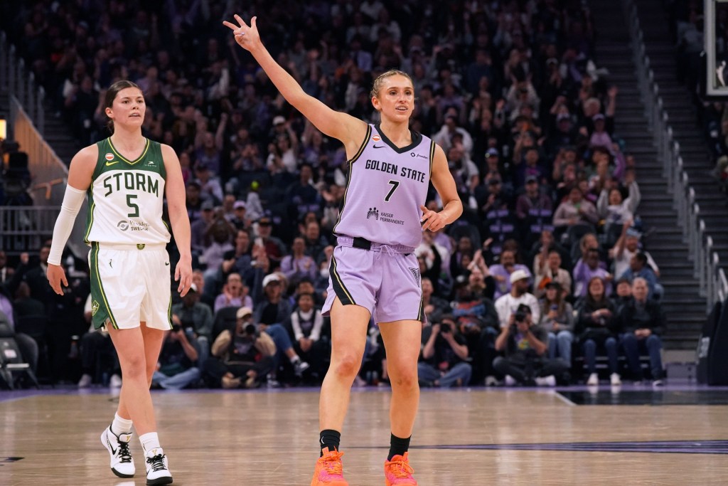 Golden State Valkyries guard Miela Sowah celebrates a 3-pointer by raising her right hand with three fingers extended. A Seattle Storm defender is behind her, looking in the direction of the basket.