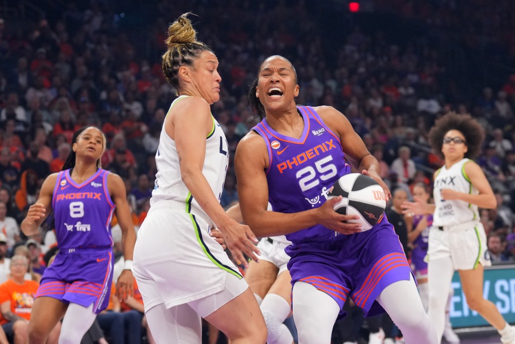 Alyssa Thomas in a purple Phoenix jersey drives past a Kayla McBride in a white jersey, holding the ball with intensity. Teammates and crowd visible in background.
