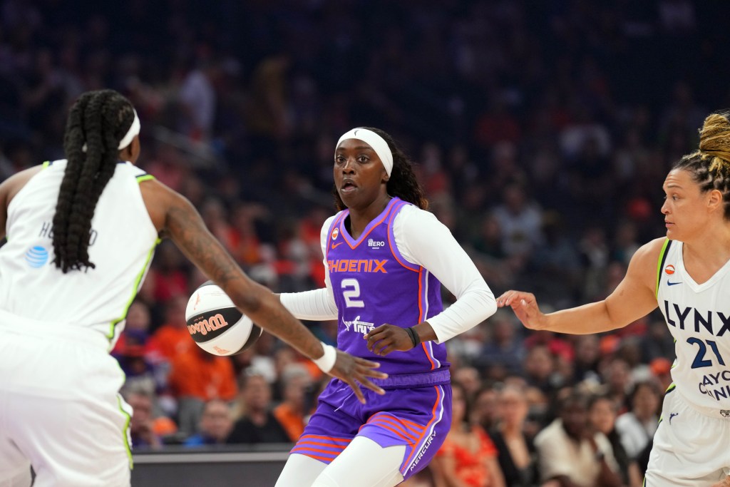 Kahleah Copper in a purple Phoenix jersey dribbles past opponents in white jerseys. The action is intense, with a crowded arena in the background.