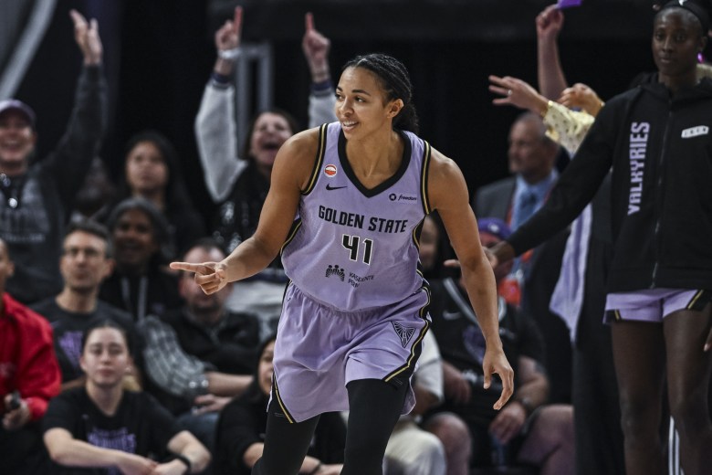 Golden State Valkyries center Kiah Stokes reacts after a three point basket. She is facing the camera and pointing to her right. The Valkyries bench and some fans are shown behind her cheering.
