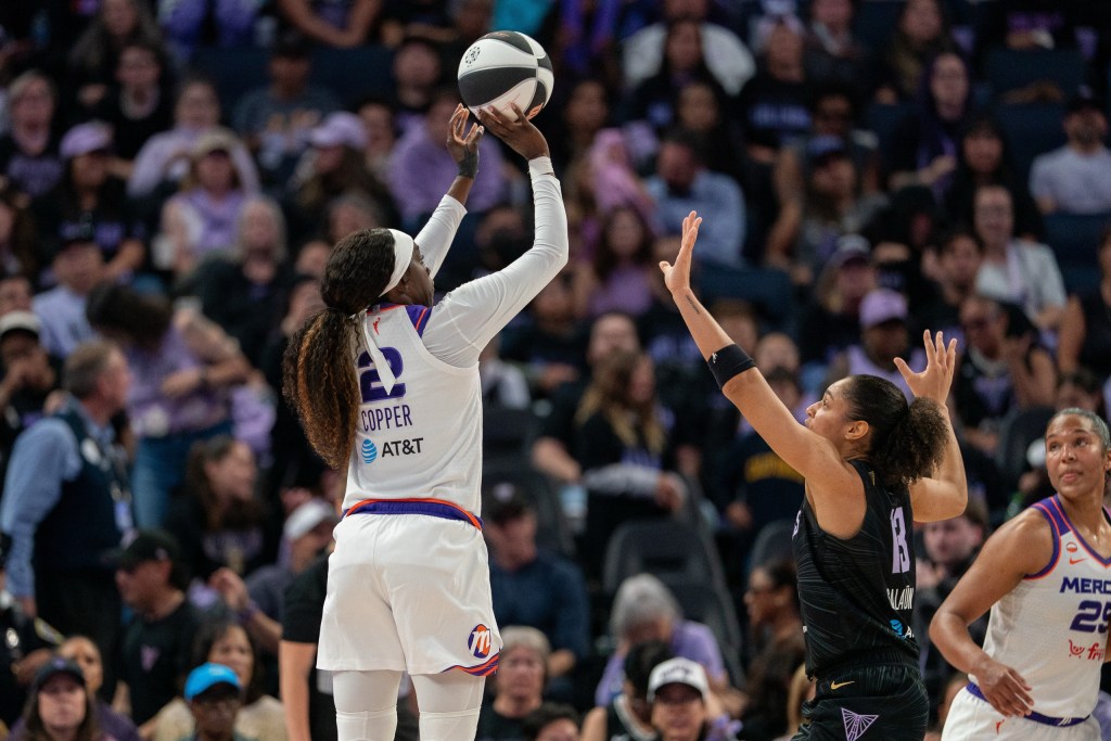 Phoenix Mercury guard Kahleah Copper shoots the ball over Golden State Valkyries forward Janelle Salaun. Both are shown from the back with a large but out of focus crowd behind them.