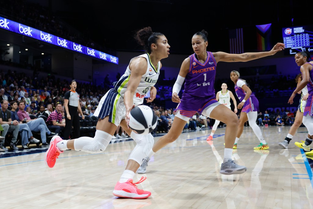 A player in a green and white jersey dribbles the ball while being challenged by a player in a purple jersey