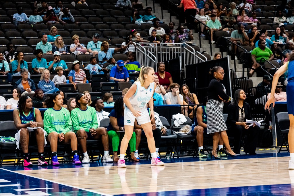 A player wearing a white uniform waits for the ball in front of a team bench.