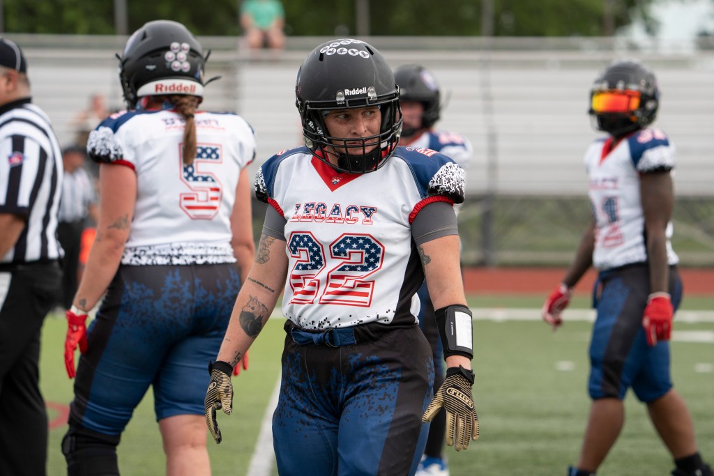 Football player with black helmet, white jersey with red, white and blue lettering. Reads "Legacy" with No. 22 in blue and white stars and red and white stripes.