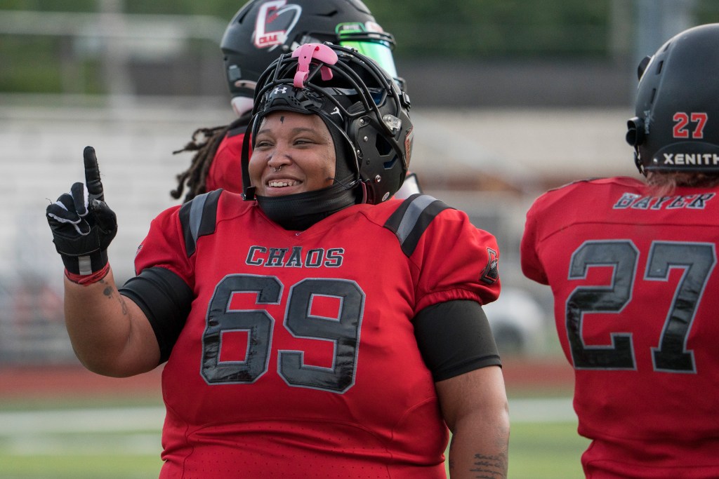 Football player holds up the index finger. Wearing red jersey that reads "CHAOS" in black font and No. 69 in black font. Player's helmet is up and sitting on top of their head
