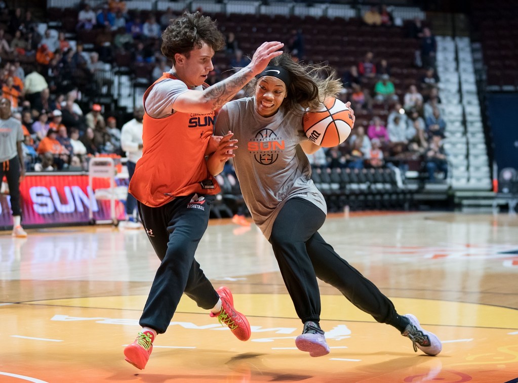 Connecticut Sun guard Harmoni Turner drives down the middle of the lane. The ball is in her left hand, and she leans to her right to ward off a practice player who's running alongside her and trying to get a hand in.