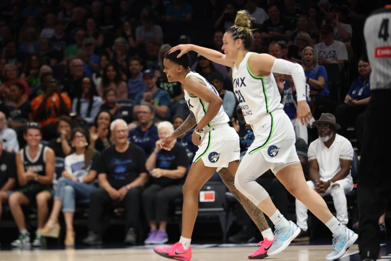 Courtney Williams and Kayla McBride laugh as they run on the court in their white Lynx jerseys as McBride pats Williams on the head