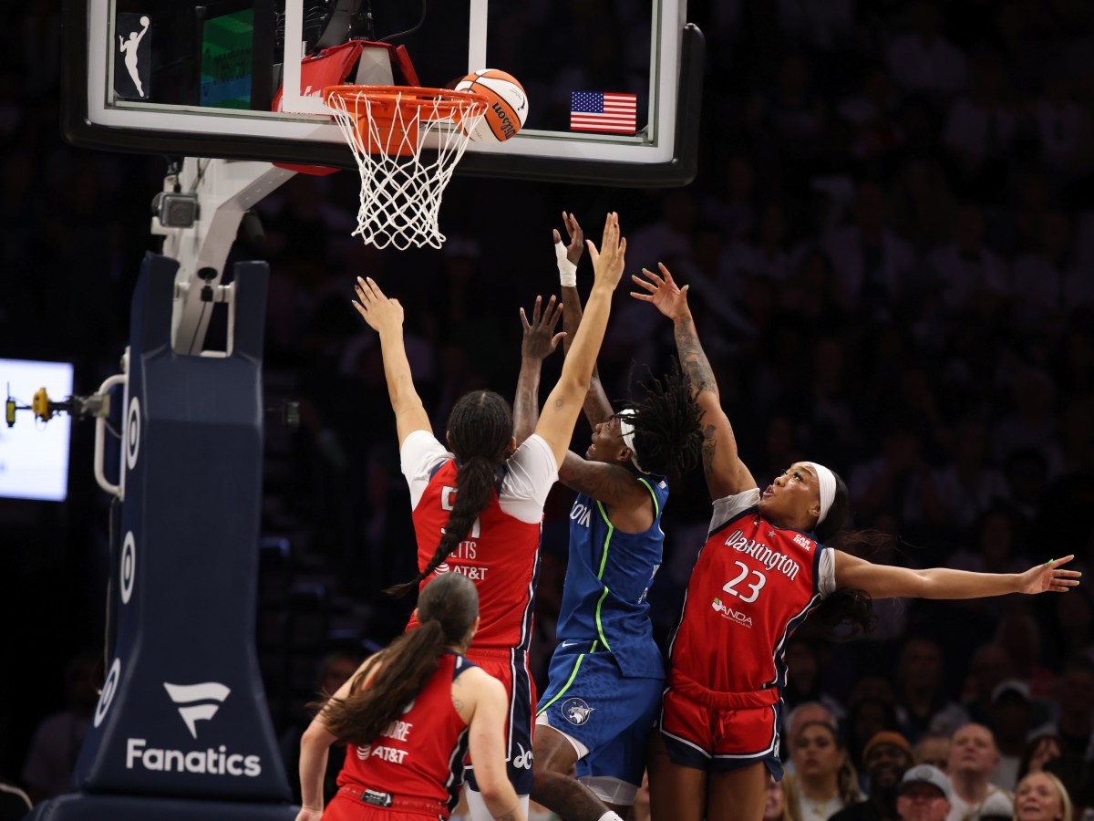 Washington Mystics center Lauren Betts has her hands straight up as she contests a shot by Minnesota Lynx forward Natasha Howard. Mystics guard Cotie McMahon tries to contest it from behind but isn't able to alter the shot. The shot is at the rim but looks like it might get stuck between the rim and the backboard.