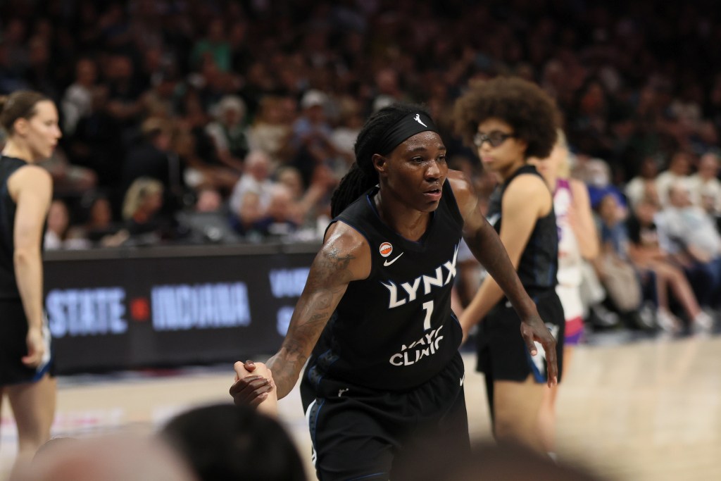 Minnesota Lynx forward Natasha Howard (1) helps another player stand during a game against the Phoenix Mercury. Other players stand in the background, the crowd watches on in the background.