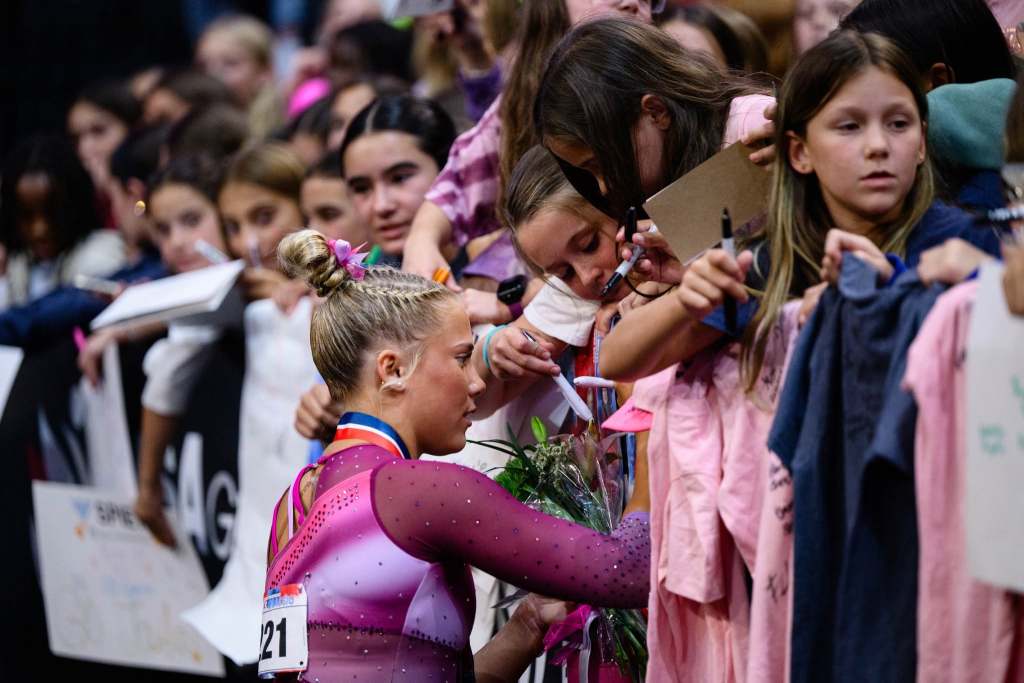 Reese Esponda wears a pink leotard and signs her autograph for a child in a crowd