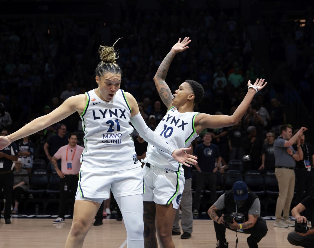 Two players in white Lynx jerseys cheer on a basketball court 