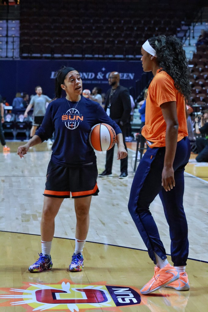 Assistant coach Ashlee McGee holds a orange and white basketball under her arm while talking to Aaliyah Edwards who is standing next to her wearing an orange warmup shirt.