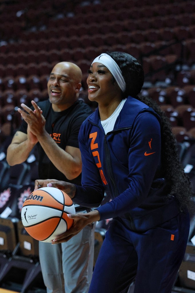 Aneesah Morrow holds an orange and white WNBA basketball while smiling and looking at the basket. Chaz Franklin stands behind her clapping and smiling.