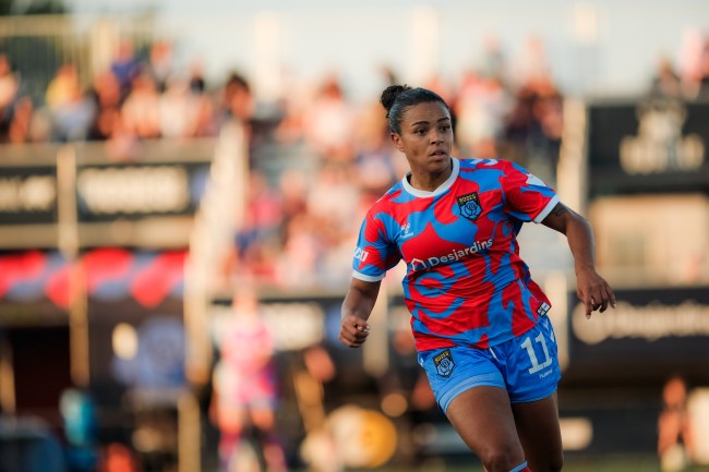 A player in a red and blue kit runs in front of stands full of fans.