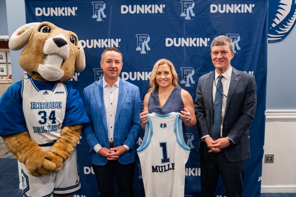Rhode Island head coach Colleen Mullen poses with a No. 1 Mullen jersey and Rhody the Ram (left), Rhode Island vice president/director of athletics Pat Lyons (second from left) and Rhode Island president Marc Parlange (right) at her introductory press conference in front of a Rhode Island backdrop.