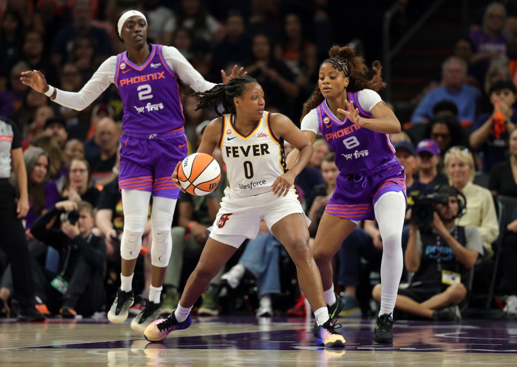 Fever guard Kelsey Mitchell dribbles while Mercury guards Kahleah Copper and Monique Akoa Makani defend, focused and intense. Crowd watches in excitement.