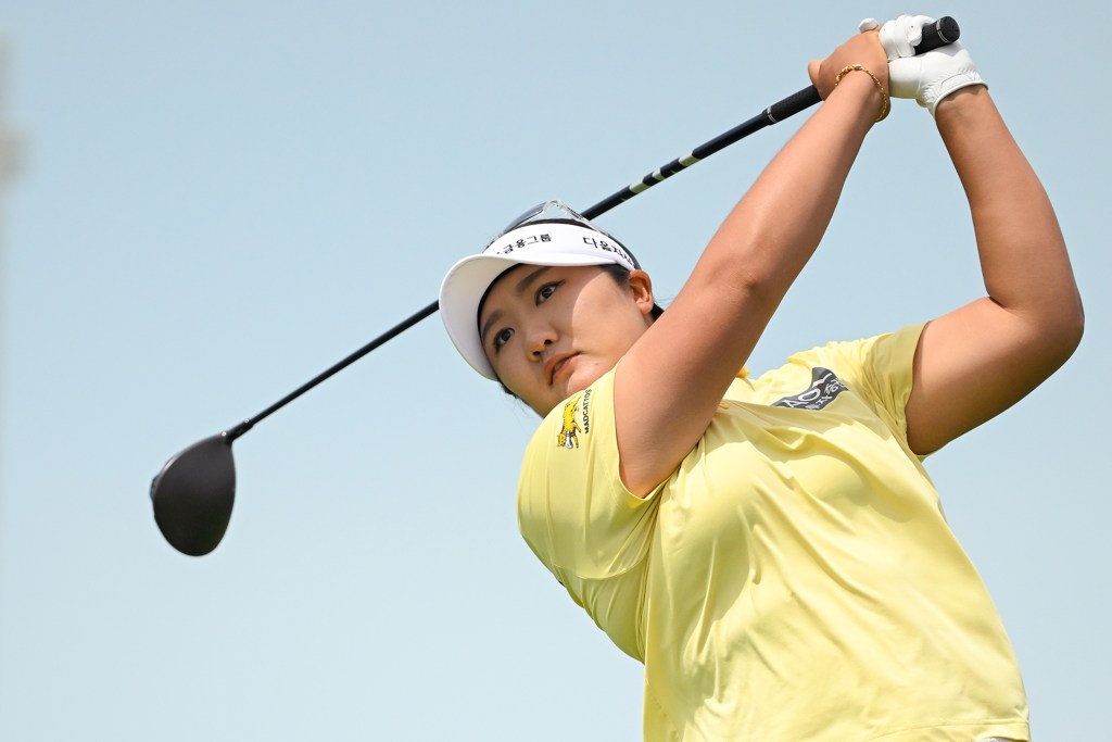 Haeran Ryu follows through on a golf shot. Her hands are up and to the left of her head, and the club wraps behind her head.