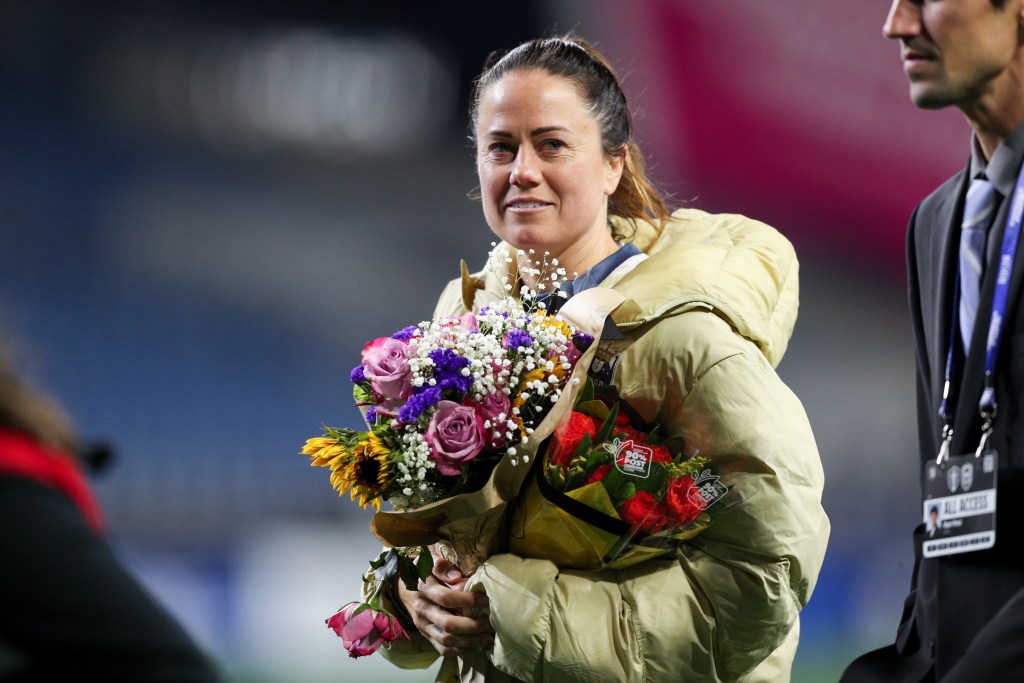 Seattle Reign FC defender Lauren Barnes holds two bouquets of flowers and looks towards the camera. Barnes is wearing a puffy coat.
