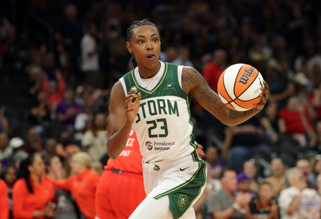 A player in a white and green Seattle Storm jersey holds onto the basketball on a court during a game. 