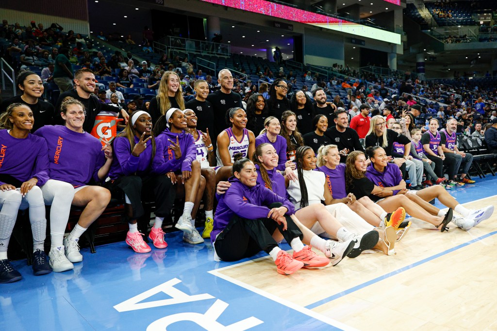 The entire Phoenix Mercury team, including players, coaches, and staff, sit and kneel together on a basketball court, posing for a group photo.