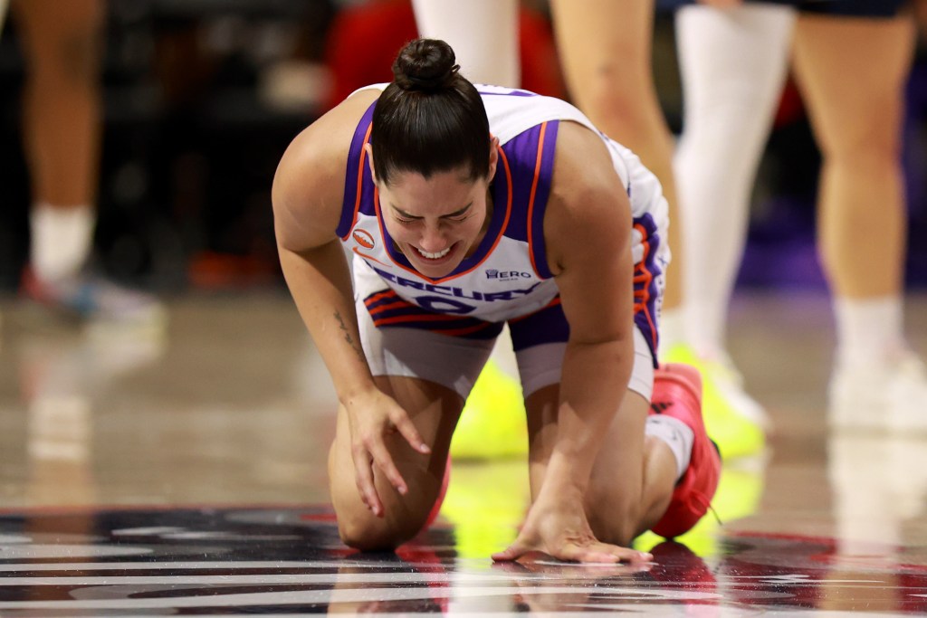 Kelsey Plum, wearing a white Mercury uniform, kneels on the court in pain after suffering an injury.