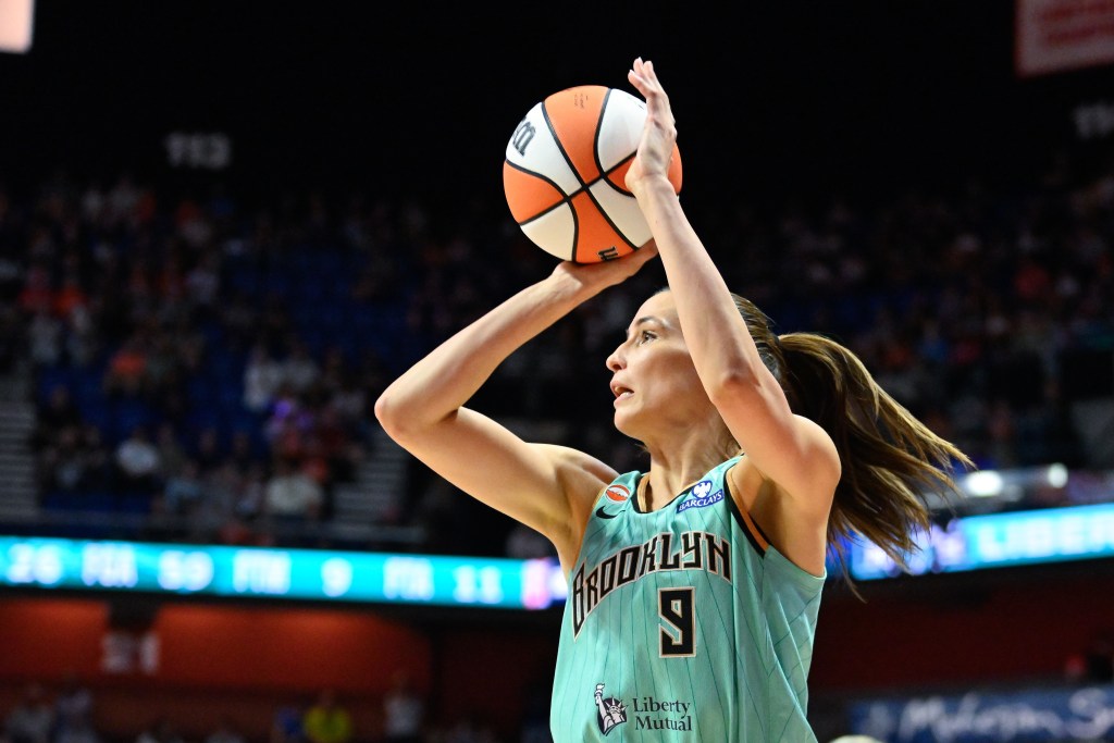 A player in a teal Brooklyn jersey winds up to shoot a basketball on a court. 