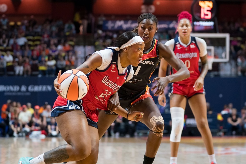 Washington Mystics guard Cotie McMahon is shown dribbling the ball with her right hand. Her defender is on her hip but unable to get fully in front of her. Mystics center Shakira Austin watches in the background.