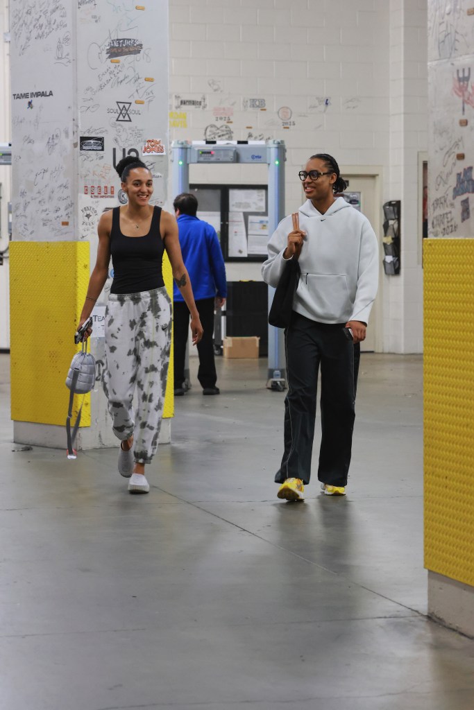 Connecticut Sun guards Nell Angloma and Leïla Lacan walk in together on game day. ANgloma is wearing a white nike hoodie, glasses and black pants while carrying a black purse. Lacan is wearing a black tank top and white sweatpants with black spots while carrying her phone in her hand.