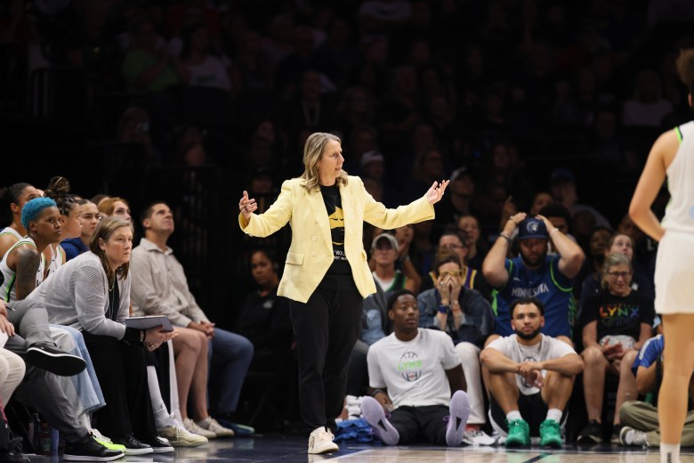 Cheryl Reeve extends her arms during a basketball game wearing a yellow blazer over a dark shirt