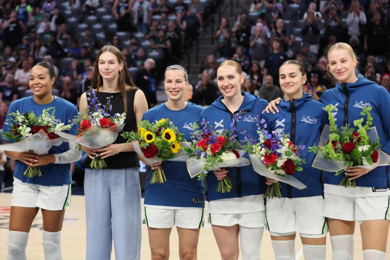 Six Minnesota Lynx stand in a horizontal row holding flowers and smiling