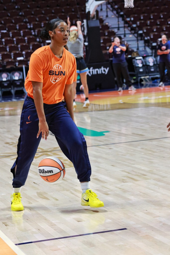 Ashlon Jackson dribbling a basketball between her legs wearing an orange warmup shirt, blue pants and yellow Nike sneakers.