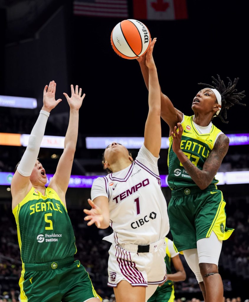 Three players jump for a basketball in the air - two in green and yellow Seattle jerseys and one in a white and purple Toronto jersey 