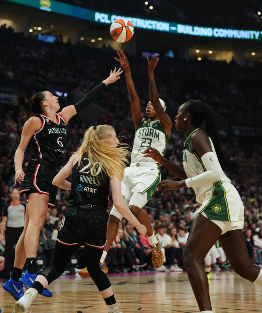 Two players in black jerseys and two players in green and white jerseys jump for a basketball 