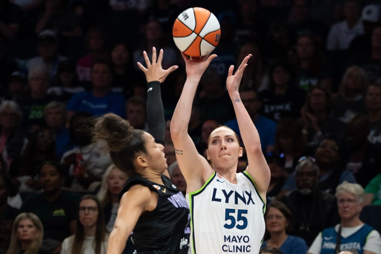 Chloe Bibby, wearing a white jersey, extends the basketball over Veronica Burton wearing black
