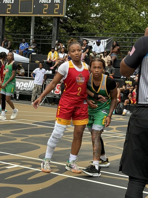 Two players one in a red uniform and another in a green uniform battle at Rucker Park.