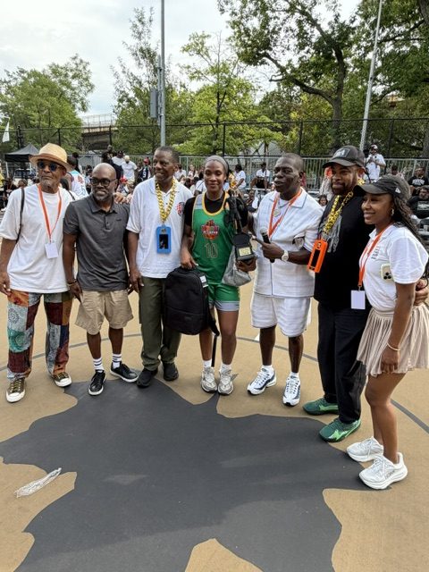 A basketball player in a green uniform is smiling as she poases for a photo with six different people.