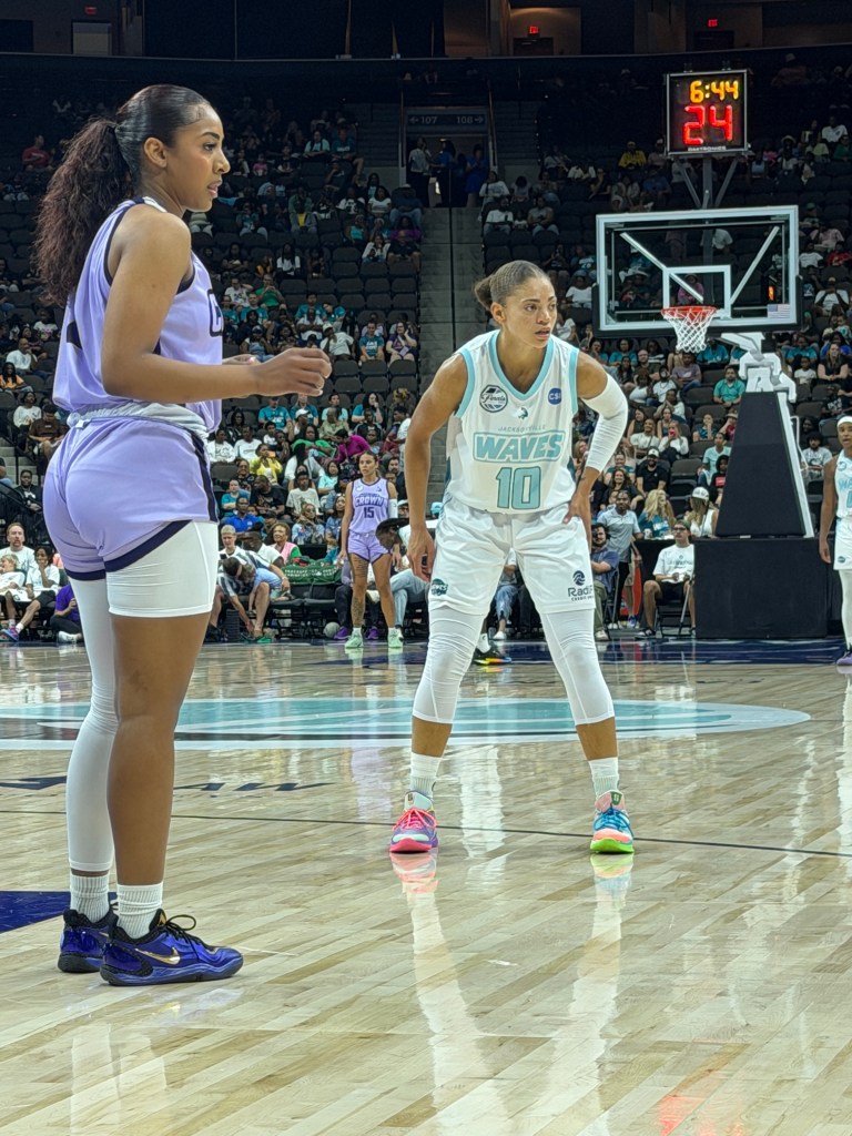 A player in a purple jersey prepares to receive the ball as she's guarded by a player in a white jersey.