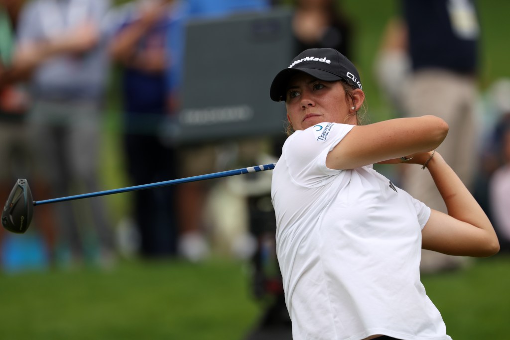 Asterisk Talley hits a tee shot and follows through on her swing. She looks after her shot and the club wraps behind her head.