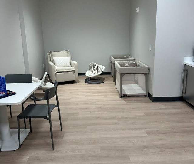 A photo of a nursery room with a nursing chair along with cribs and a table with games.