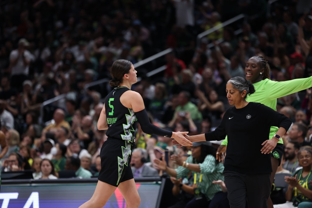 A player in black and green bumps hands with the coach in all black.