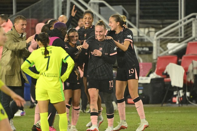 Players in black celebrate. A coach in a trench coat smiles behind them. A player in yellow stands, dejected, in front of them.