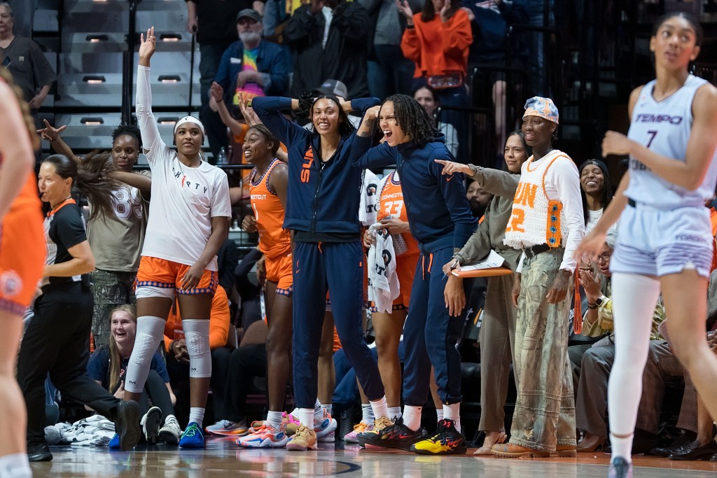 The Connecticut Sun bench standing uo with their arms in the air smiling and celebrating a teammates play during the game.