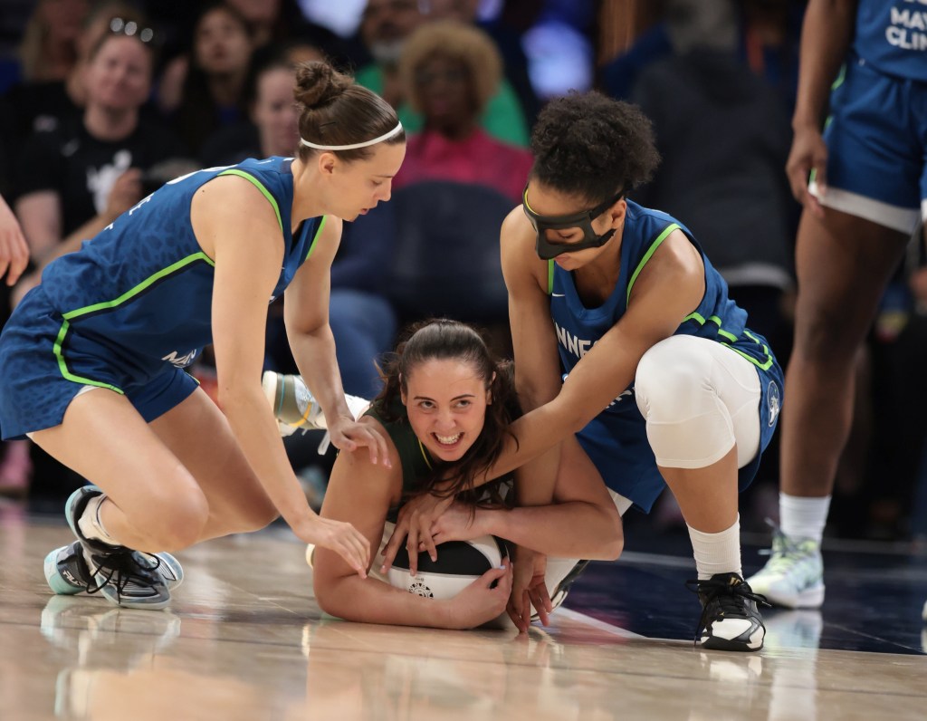 Mackenzie Holmes tightly grips the ball between her chest and the floor, grimacing while a Minnesota Lynx defender on either side of her try to reach in and take it from her.