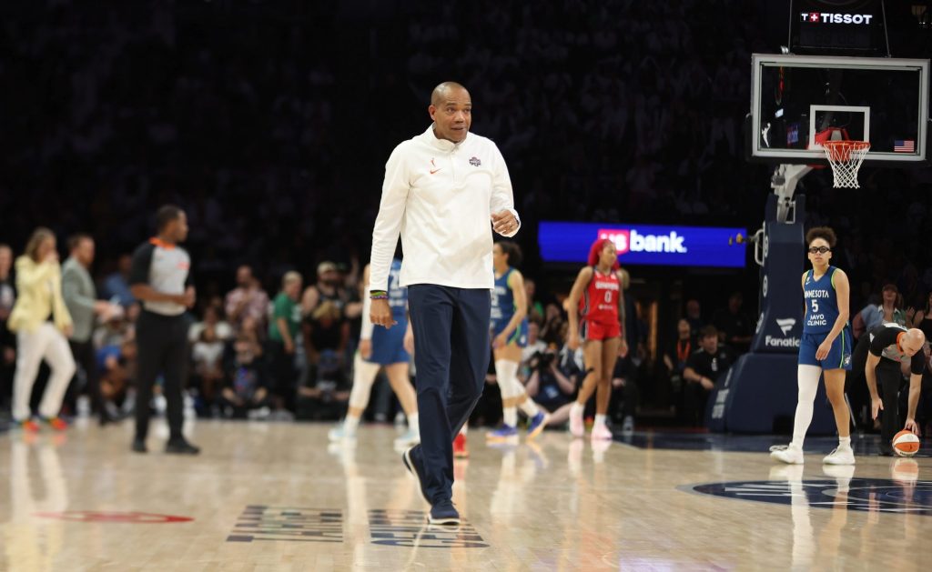 Washington Mystics head coach Sydney Johnson walks onto the court. He is smiling and looking straight ahead.