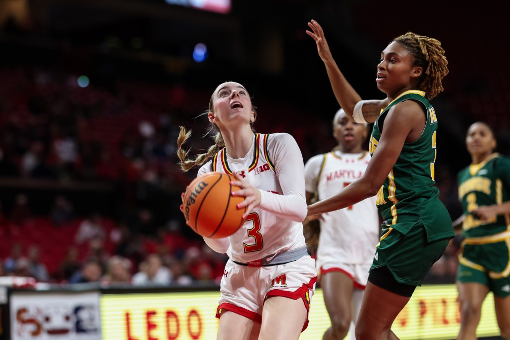 Addi Mack wearing a white shirt goes up for a shot while being guarded by a player in a green uniform who has an arm raised.