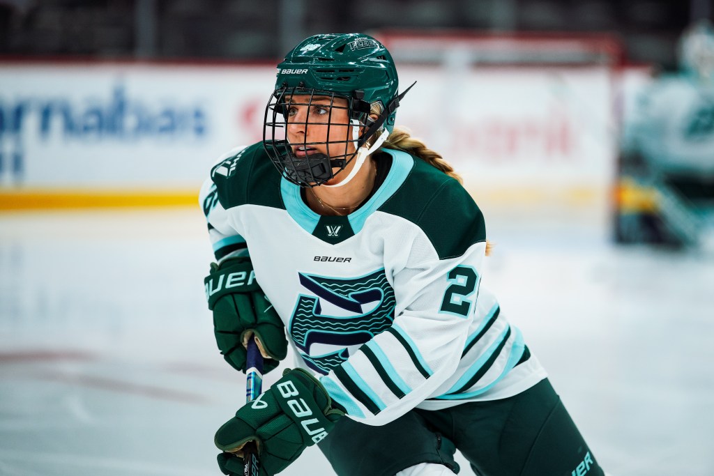 A waist-up shot of Huber looking up ice as she skates. She is wearing a white away uniform.